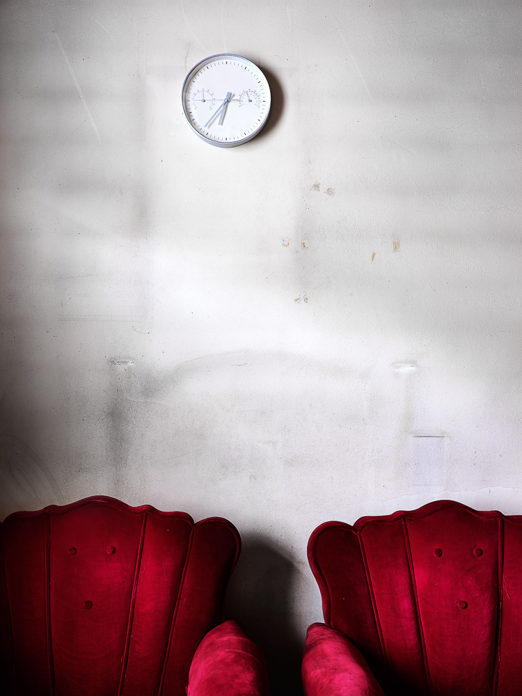 dos sillones rojos contra pared y reloj analógico