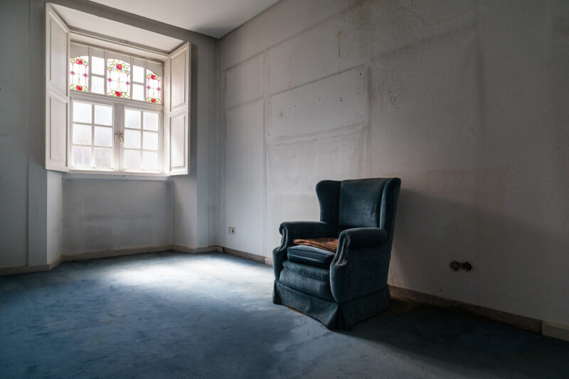habitación sin muebles excepto un sillón azul con moqueta azul y vidriera