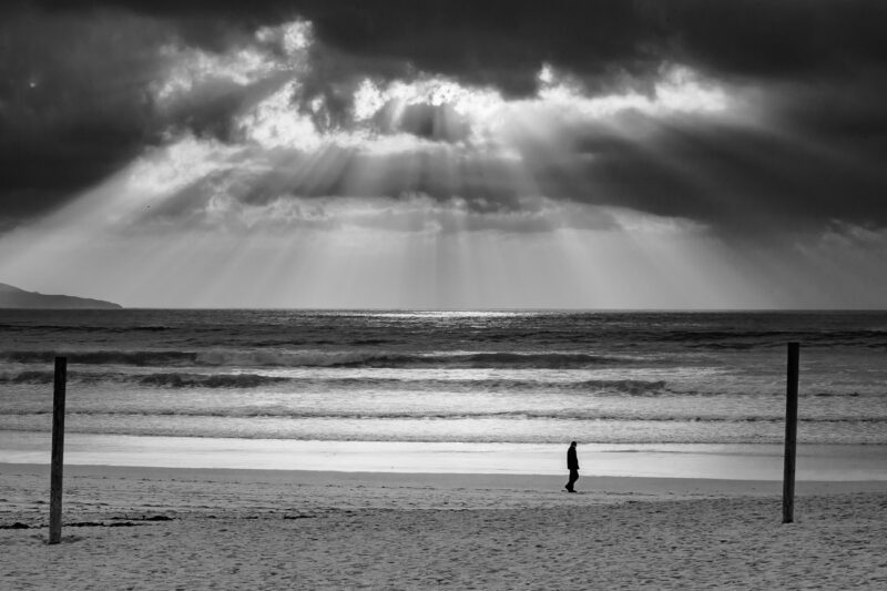 hombre caminando en la playa con rayos de sol atravesando nubes a lanzada ons