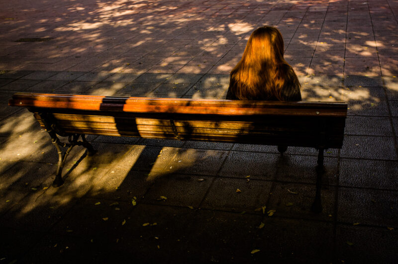 mujer pelirroja de espaldas sentada en un banco