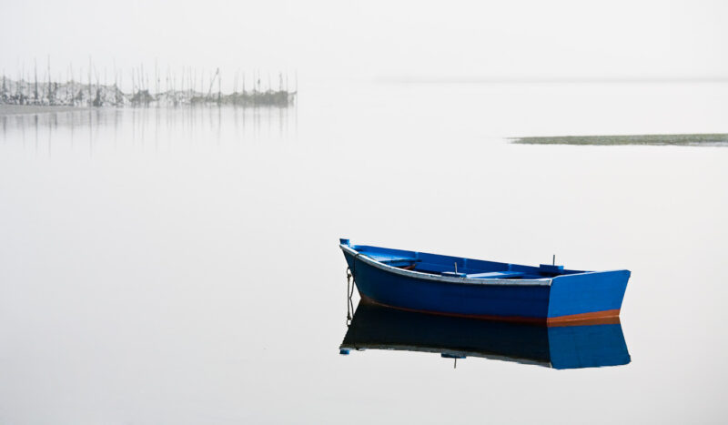 el mar y el espejo barca azul con reflejo con niebla mar