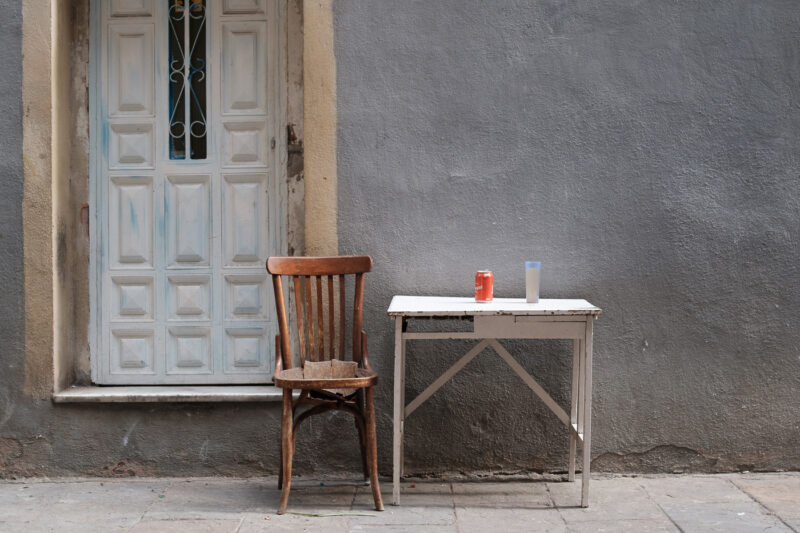 silla de madera con mesa blanca vaso y lata de refresco en la calle